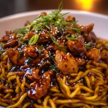 Sticky garlic chicken noodles garnished with herbs and served in a bowl.